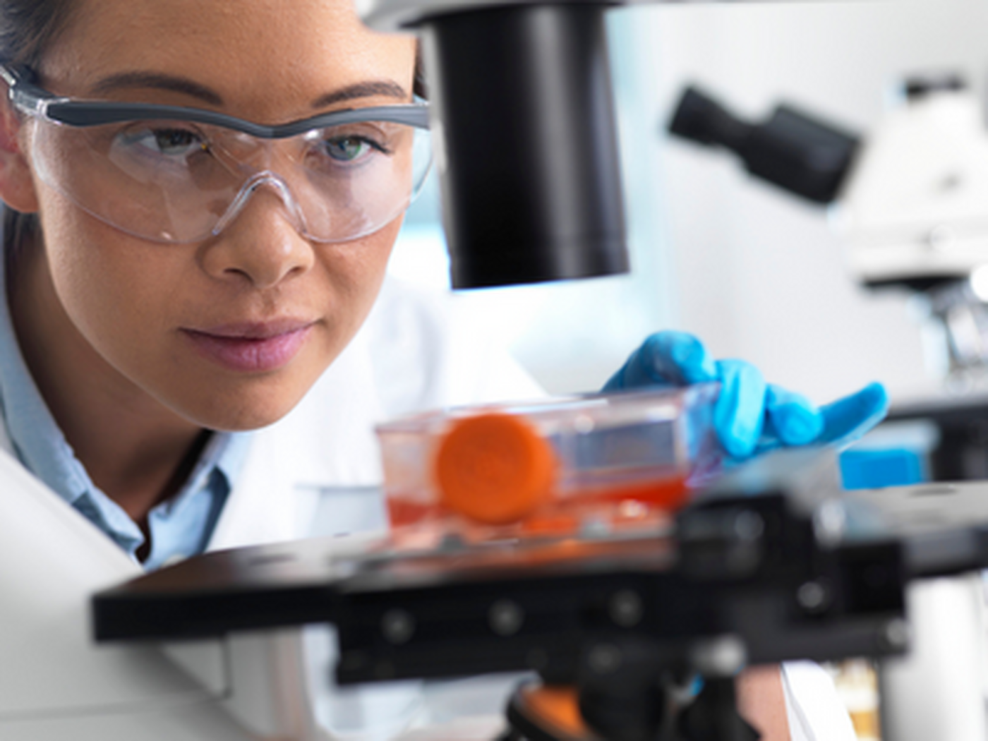 A female scientist in a lab coat observing an object in a laboratory setting.