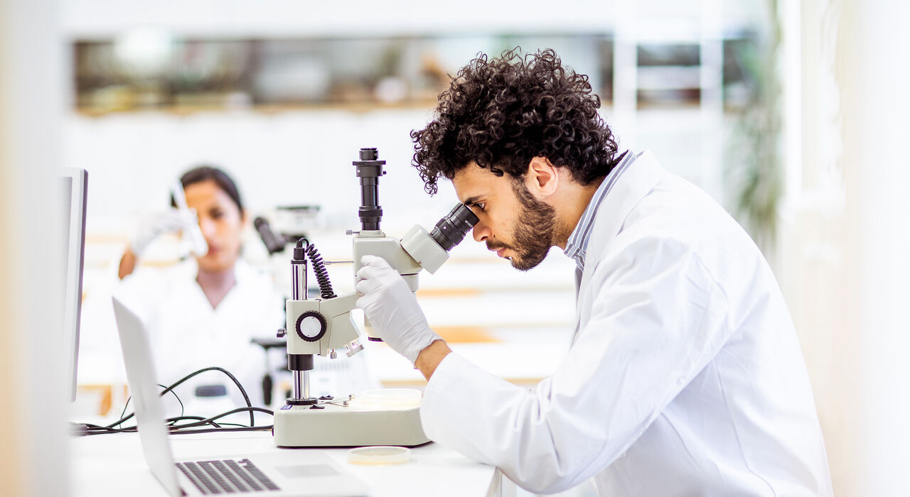 A male scientist examining a specimen through in microscope.