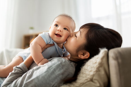 A mother gently holding and kissing her baby on the cheeks.